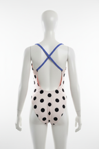 Girls white and black polka dot open-back one-piece swimsuit back view showing blue X-cross straps and orange lining